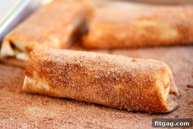 Crispy Chocolate Strawberry Cheesecake Chimis 5 Chocolate Strawberry Cheesecake Chimichangas being rolled in cinnamon sugar mixture, showing the final coating step.