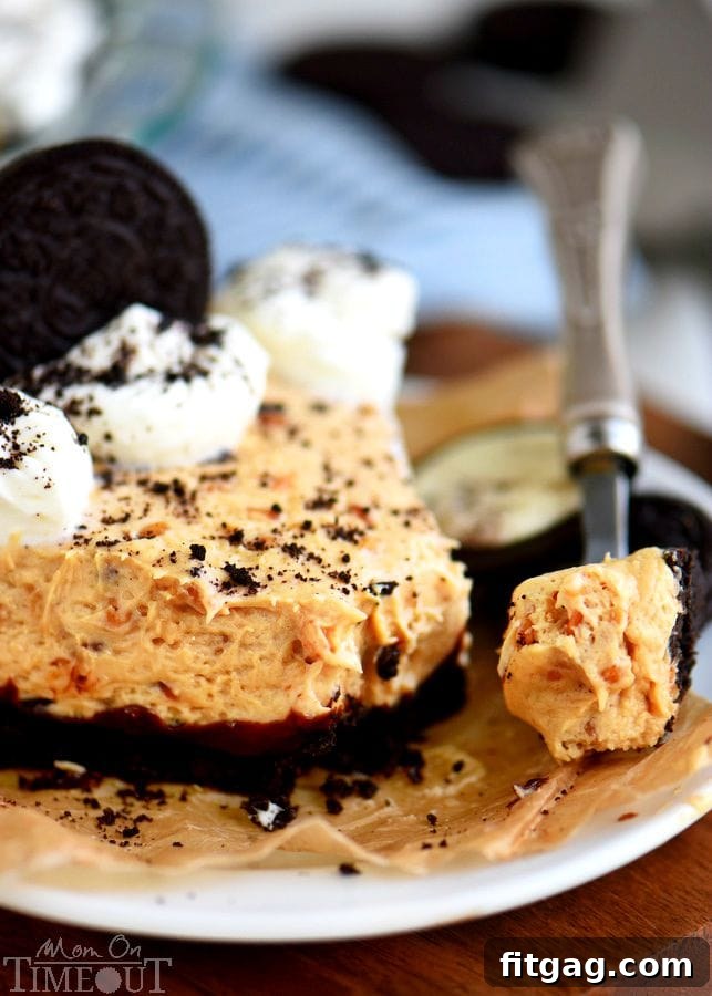 A slice of the No Bake Peanut Butter Cheesecake Pie being lifted from the dish with a fork, showing the creamy filling, hot fudge layer, and OREO crust.