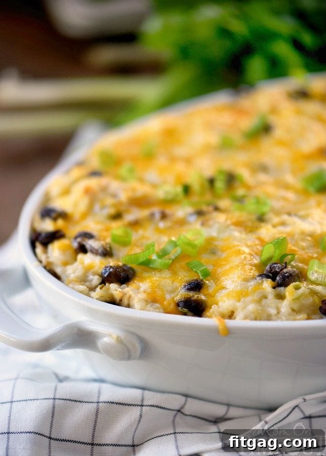 Fiesta Chicken and Rice Bake 3 Close-up of a serving of Mexican Chicken and Rice Casserole on a white plate, showing the layers of cheesy chicken, rice, and beans. A sprig of fresh cilantro is a garnish, highlighting the freshness and appeal of this comfort food casserole.