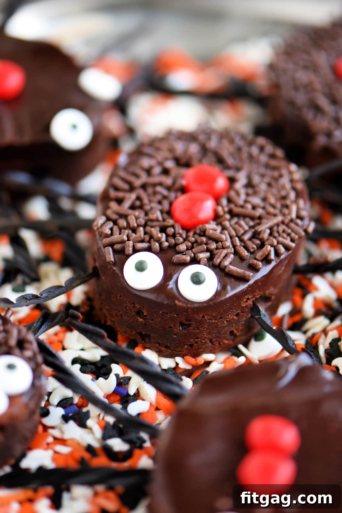 Black Widow's Midnight Fudge Bites 2 Decadent Black Widow Brownie Bites with chocolate ganache, candy eyes, and licorice legs, resting on a bed of vibrant Halloween sprinkles.
