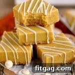 Pumpkin Fudge bars stacked on top of a decorative log with white chocolate pieces spread out.