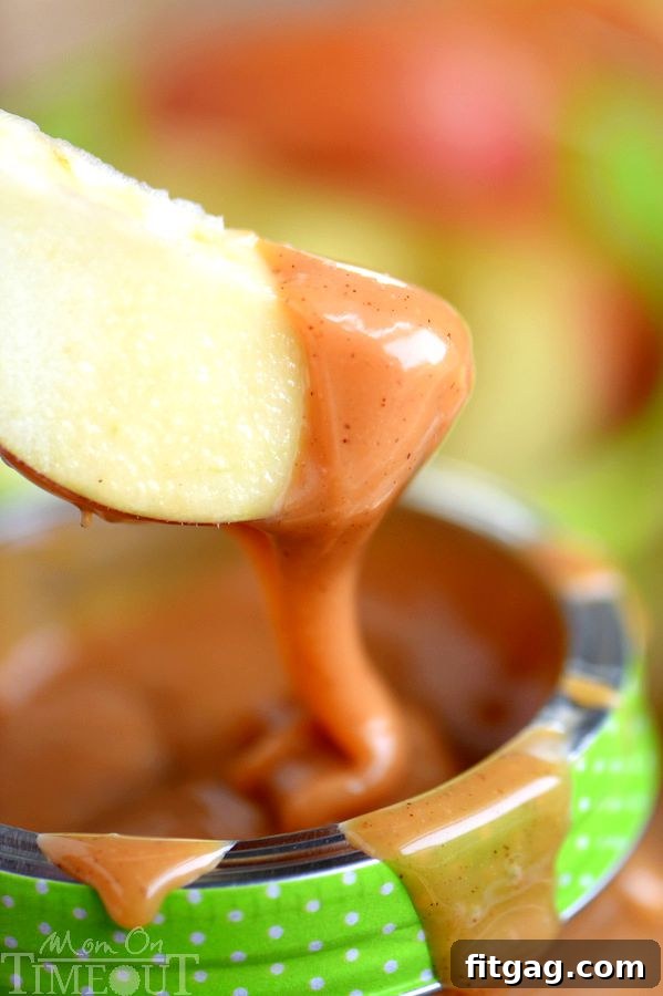 A freshly sliced apple being generously dipped into a bowl of creamy Pumpkin Spice Caramel Apple Dip, showcasing its luscious texture.
