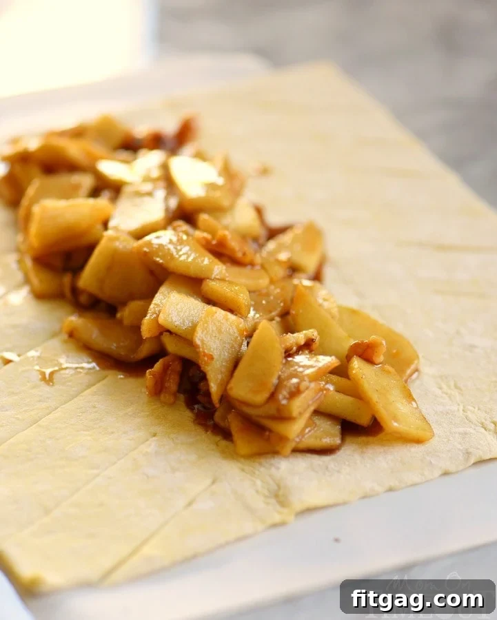 Unbaked Apple Strudel, showing the apple filling layered on puff pastry with neatly folded criss-cross strips on top.