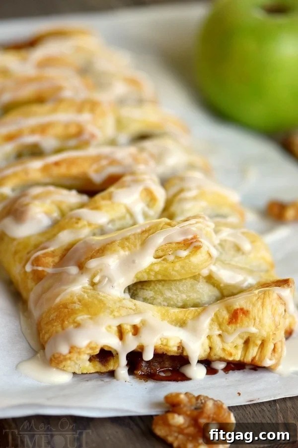 A generous slice of Apple Strudel on a small white plate, drizzled with glaze, showing the layers of apples and flaky pastry.