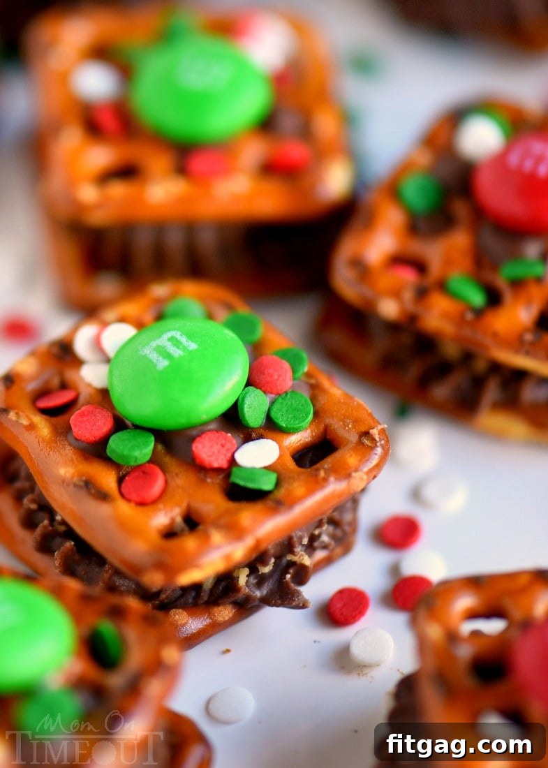 A tray of Reese's Holiday Pretzel Bites cooling on parchment paper after being topped with M&Ms and sprinkles, ready for the fridge.