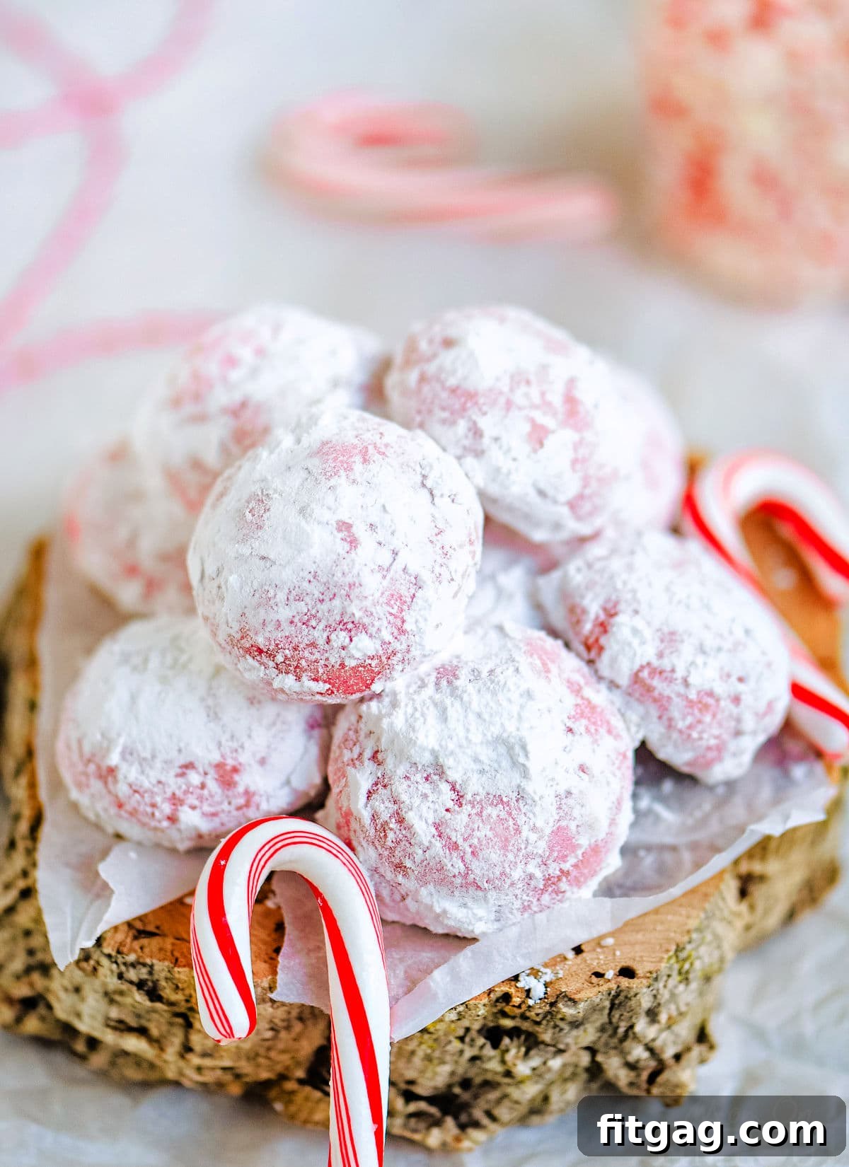 snowball cookies rolled in powdered sugar and piled on small wood block with mini candy canes scattered around it