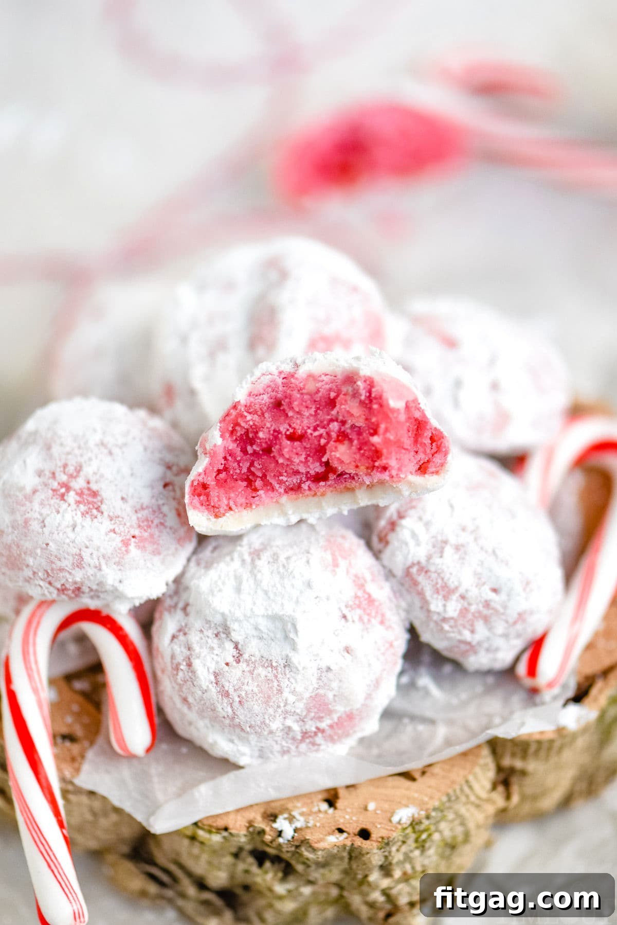 peppermint snowball cookie with bite taken sitting on top of a pile of more cookies with two candy canes on either side