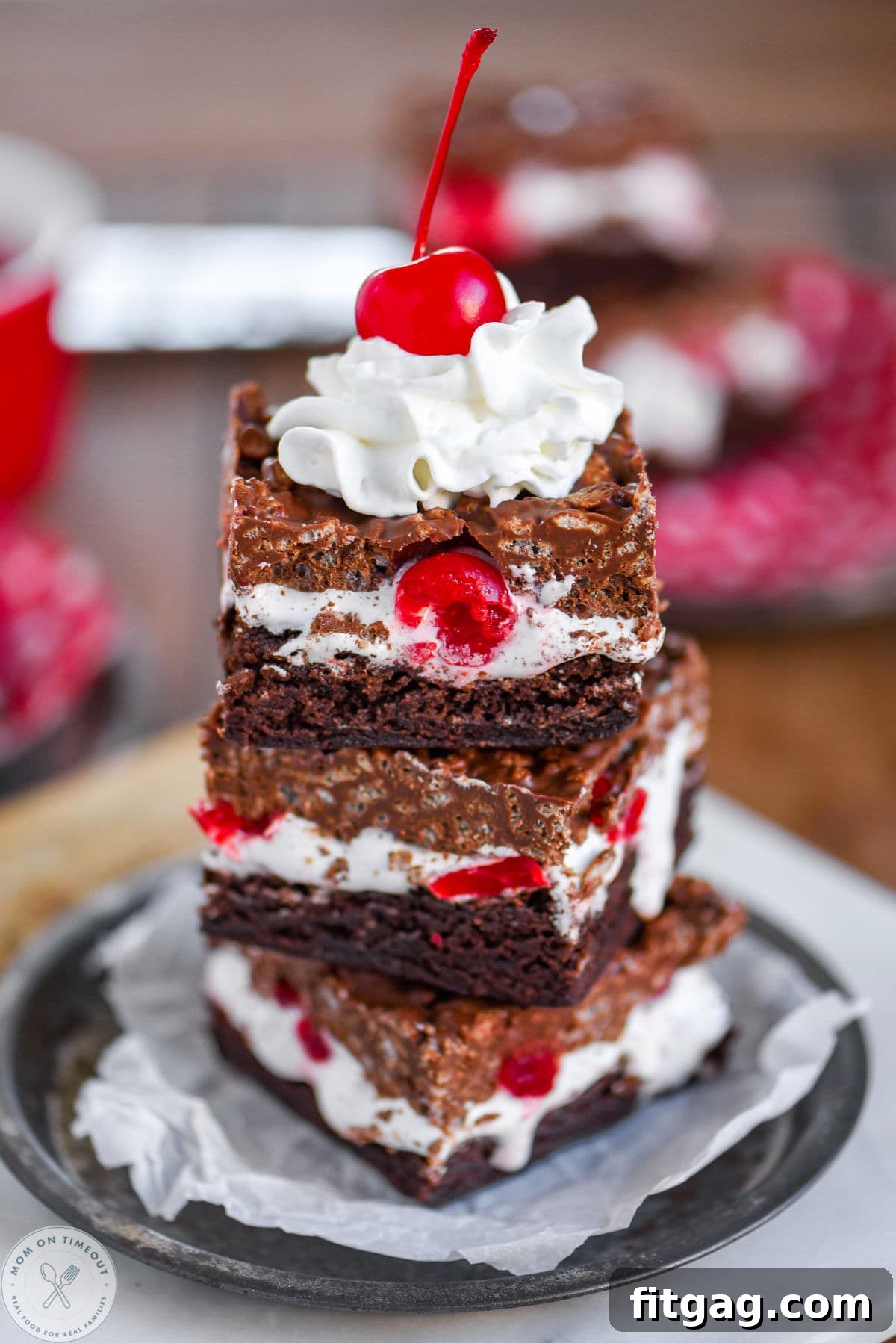 Cherry Brownie Bliss Bars 7 Three cherry dream bars stacked on parchment lined metal round plate, garnished with whipped cream and a maraschino cherry.