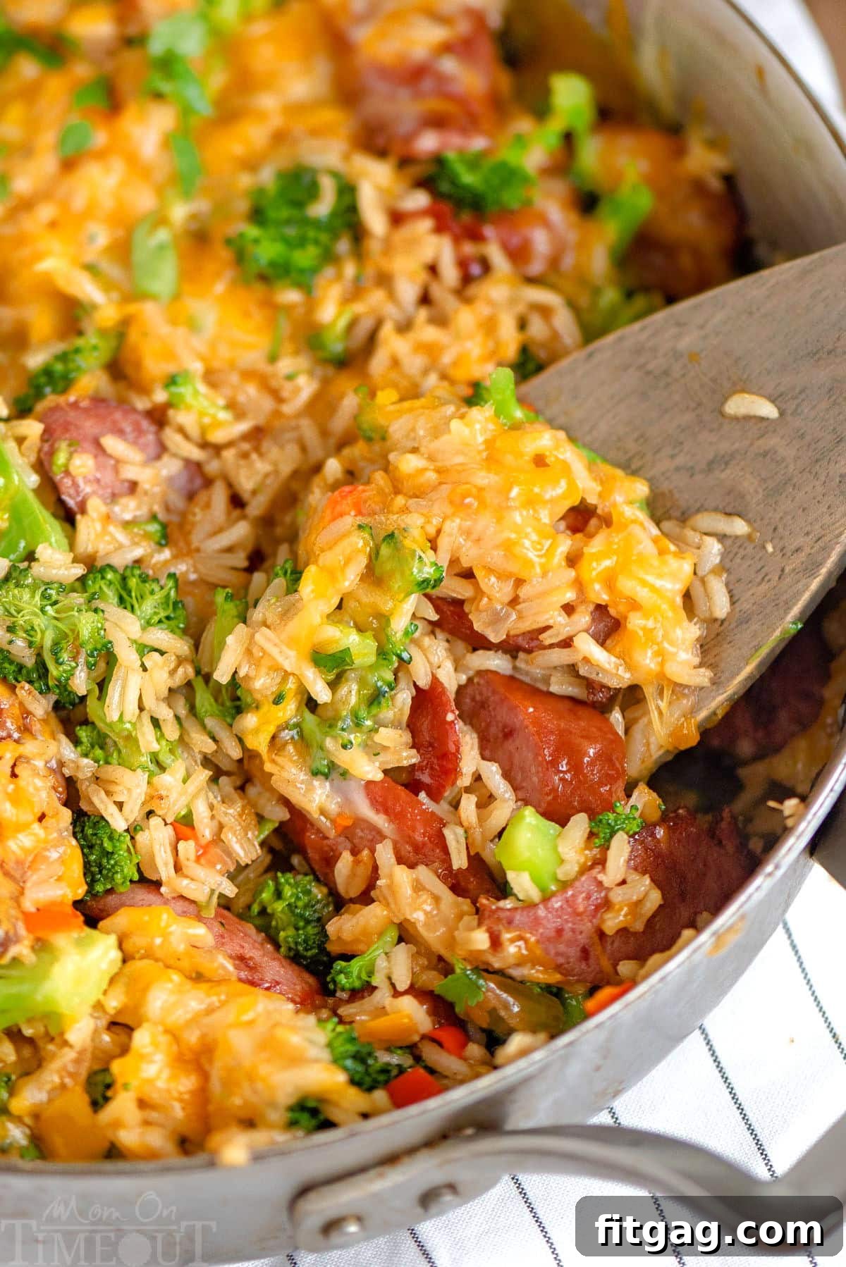 One-Skillet Cheesy Kielbasa and Broccoli Rice 5 Wood spoon scooping out kielbasa skillet with rice and broccoli.