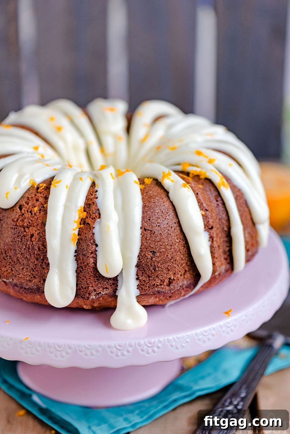 A stunning Hummingbird Bundt Cake, gracefully adorned with a light cream cheese frosting drizzled artfully over its ridges, elegantly presented on a pink cake stand.
