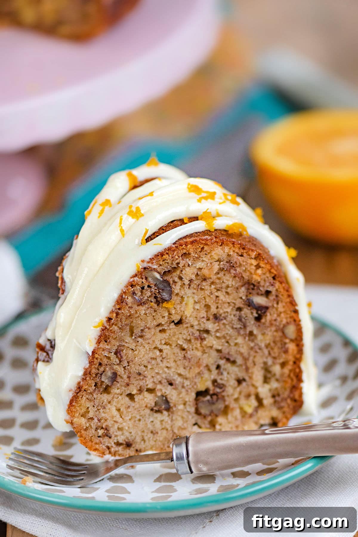 A meticulously baked Hummingbird Bundt Cake, featuring a golden-brown crust and a generous application of cream cheese frosting, sits on a small dessert plate, ready to be enjoyed.