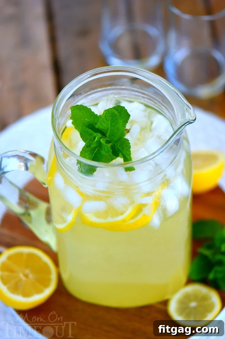 A beautiful pitcher of Party Perfect Mint Lemonade, brimming with ice, delicate lemon slices, and fresh mint sprigs, glistening and ready to serve at a gathering.