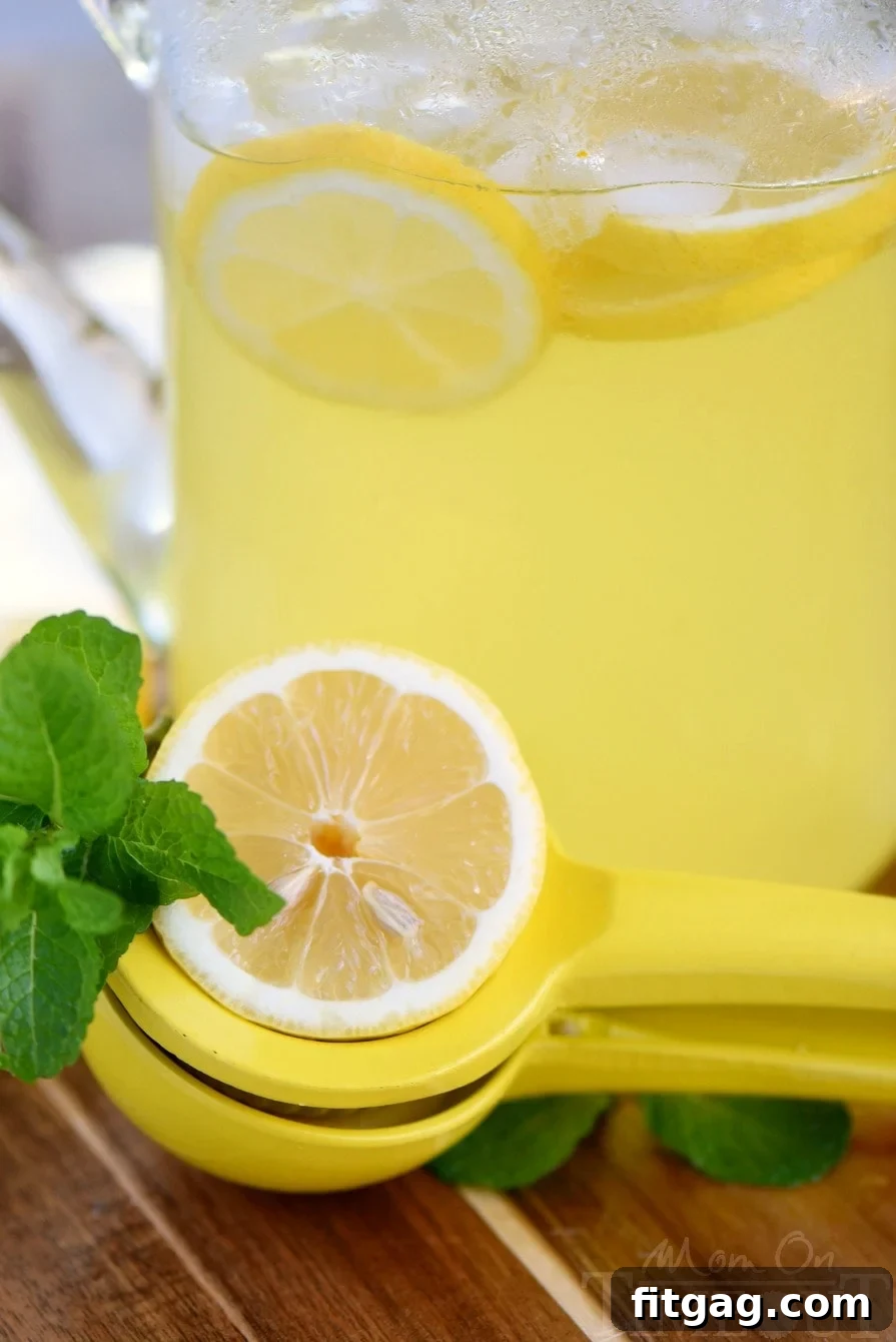 A close-up of a glass filled with Party Perfect Mint Lemonade, featuring a straw, vibrant green mint leaves, and bright yellow lemon slices, emphasizing its inviting and cool appearance.