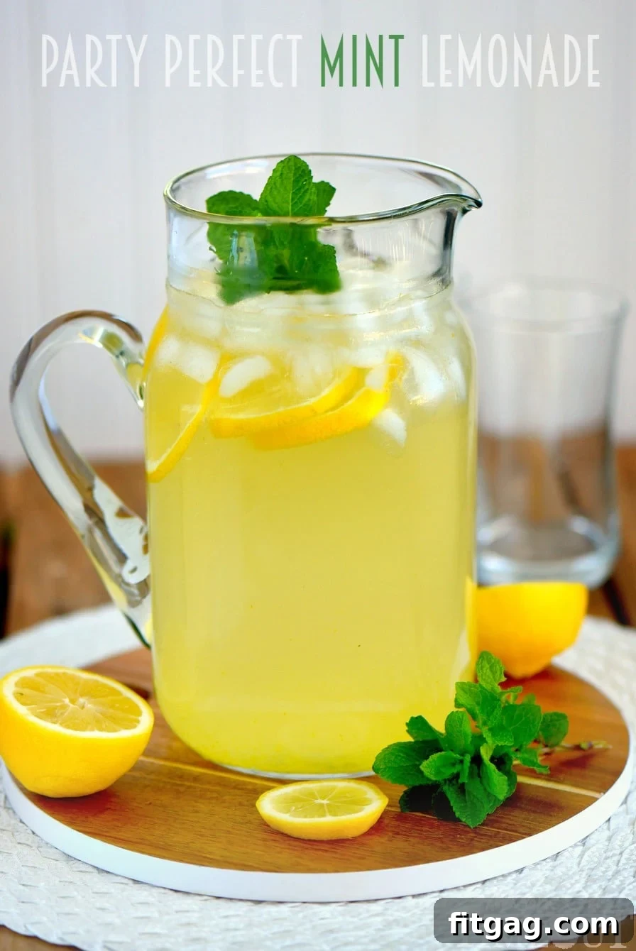 Another perspective of the pitcher and a glass of Party Perfect Mint Lemonade, artfully styled with fresh lemons and mint, set on a bright surface for a party scene.