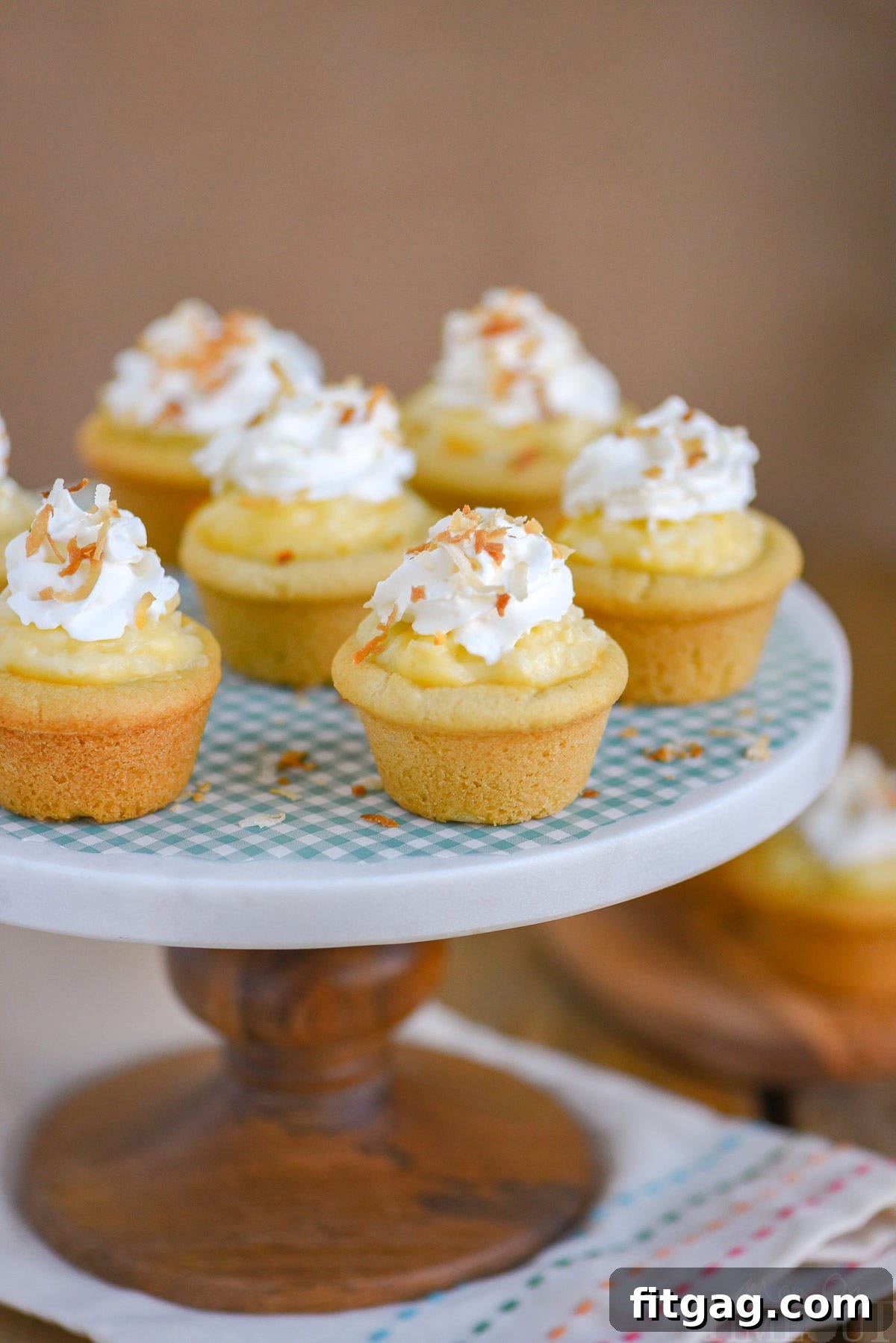 Six mini coconut cream pie cookie cups on a marble cake stand with wood base.