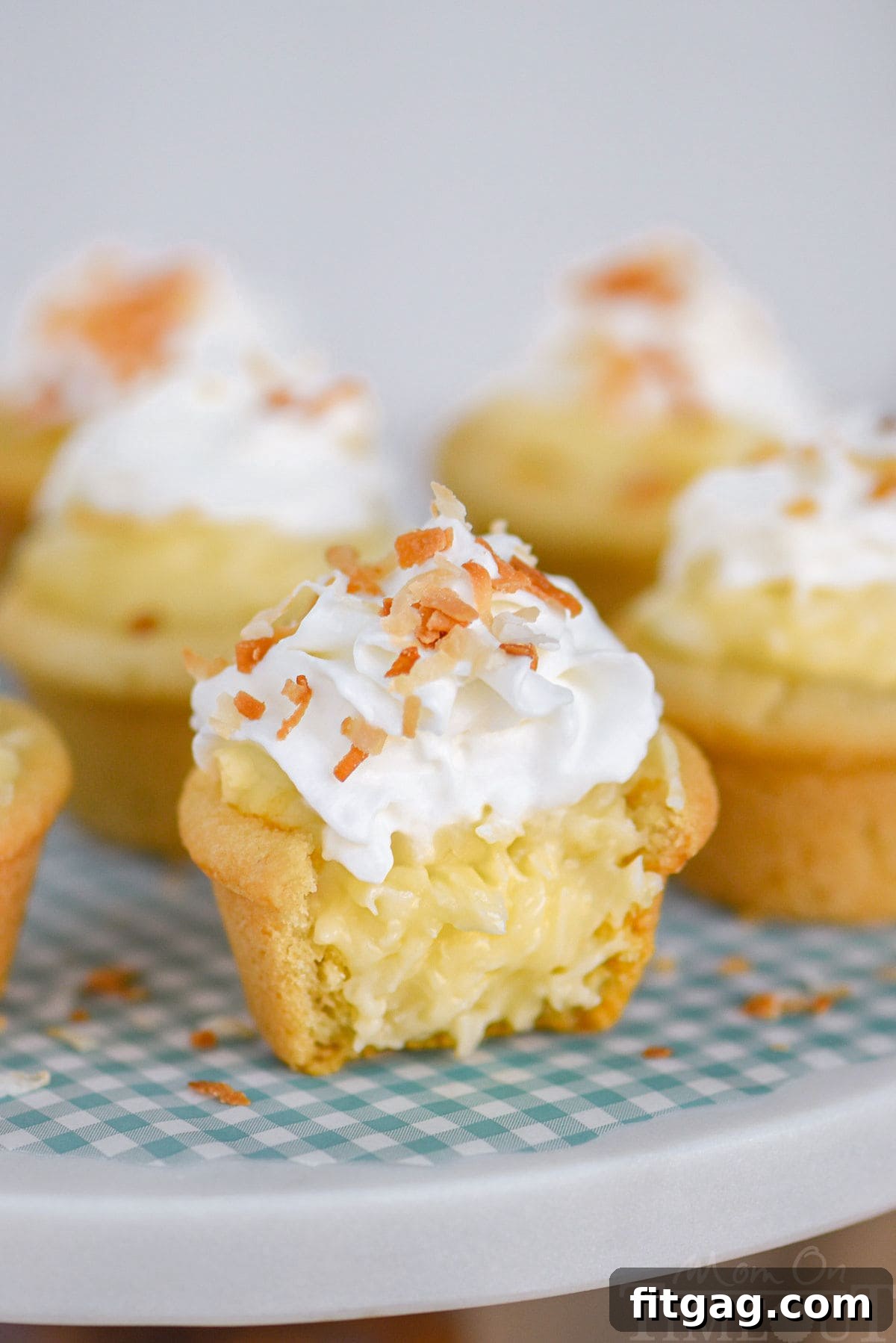 Coconut cream pie cookie cups made with sugar cookie dough are sitting on a marble cake stand and are topped with whipped cream and toasted coconut. The cup in the front has been cut in half.