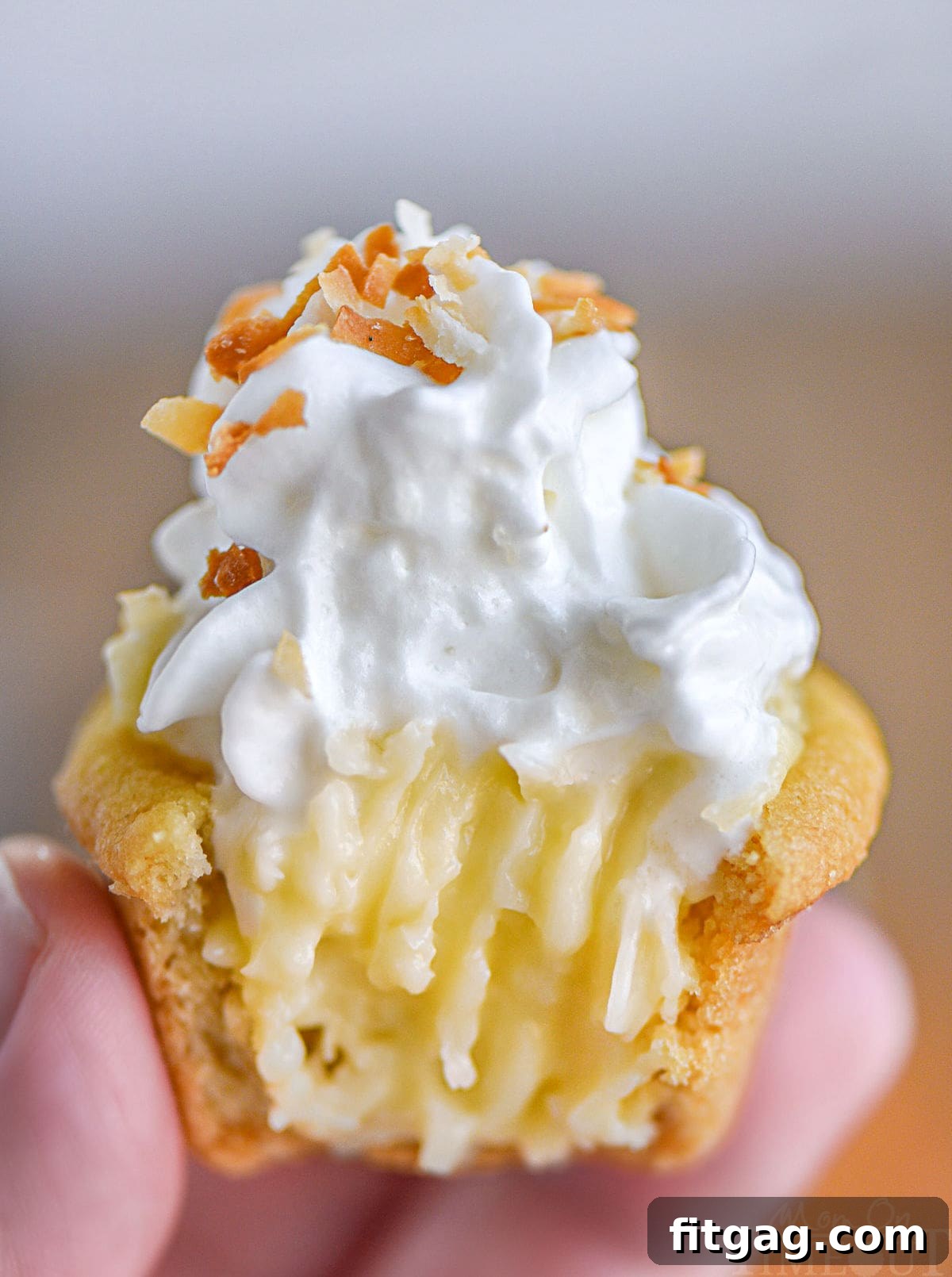 Hand holding up a mini coconut cream pie cookie cup with a bite taken out of it.