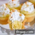 Four mini coconut cream pies on glass cake stand topped with whipped cream and toasted coconut. The front one has a bite taken out of it.