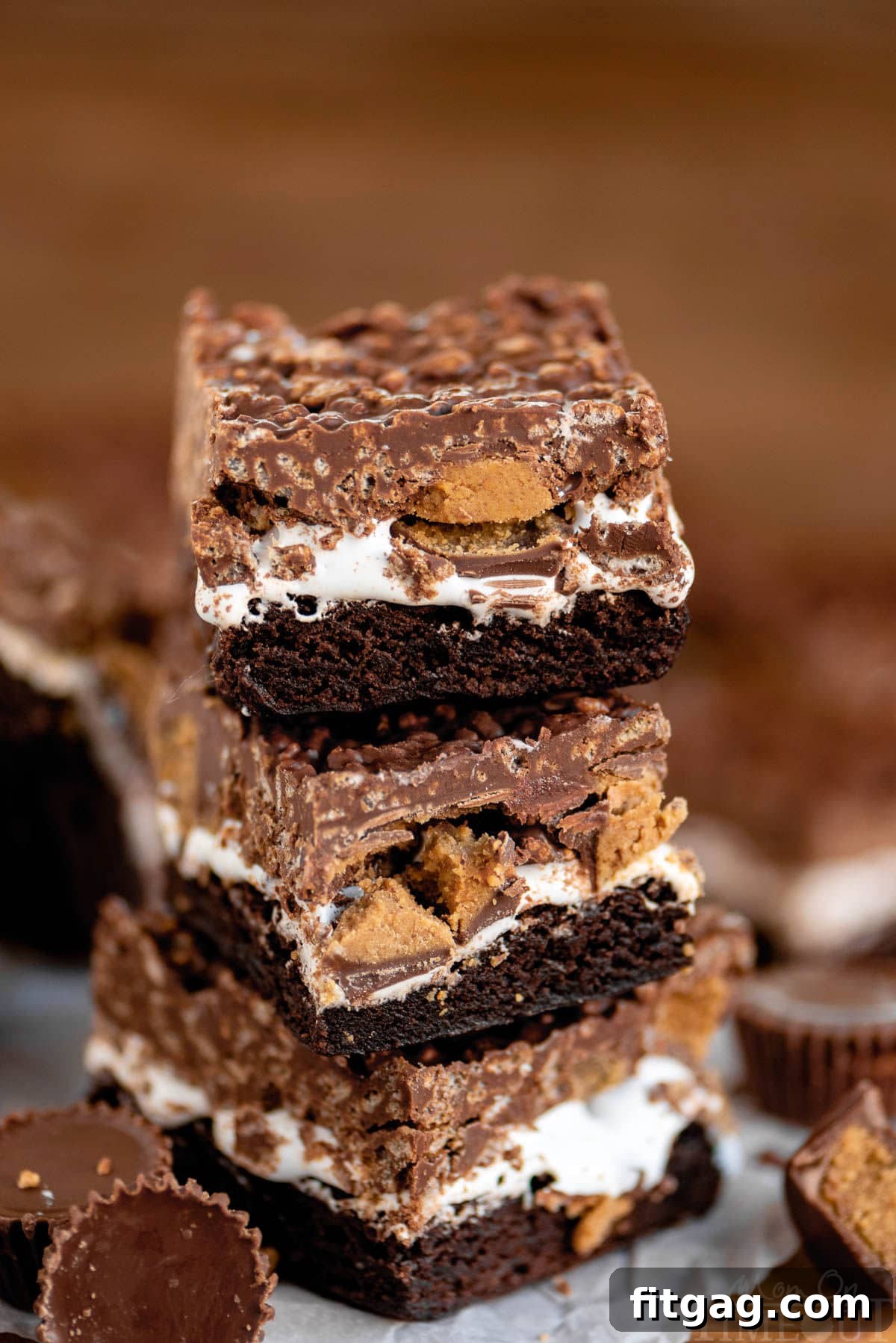 Peanut Butter Cup Marshmallow Brownies 2 Three brownies stacked on each other showcasing the distinct layers: fudgy brownie, fluffy marshmallow creme, halved Reese's peanut butter cups, and a crunchy chocolate peanut butter crispy rice topping.