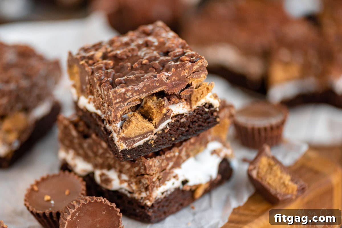 Peanut Butter Cup Marshmallow Brownies 4 A stack of two Reese's Marshmallow Brownies with Reese's peanut butter cups scattered around, highlighting the rich colors and textures.