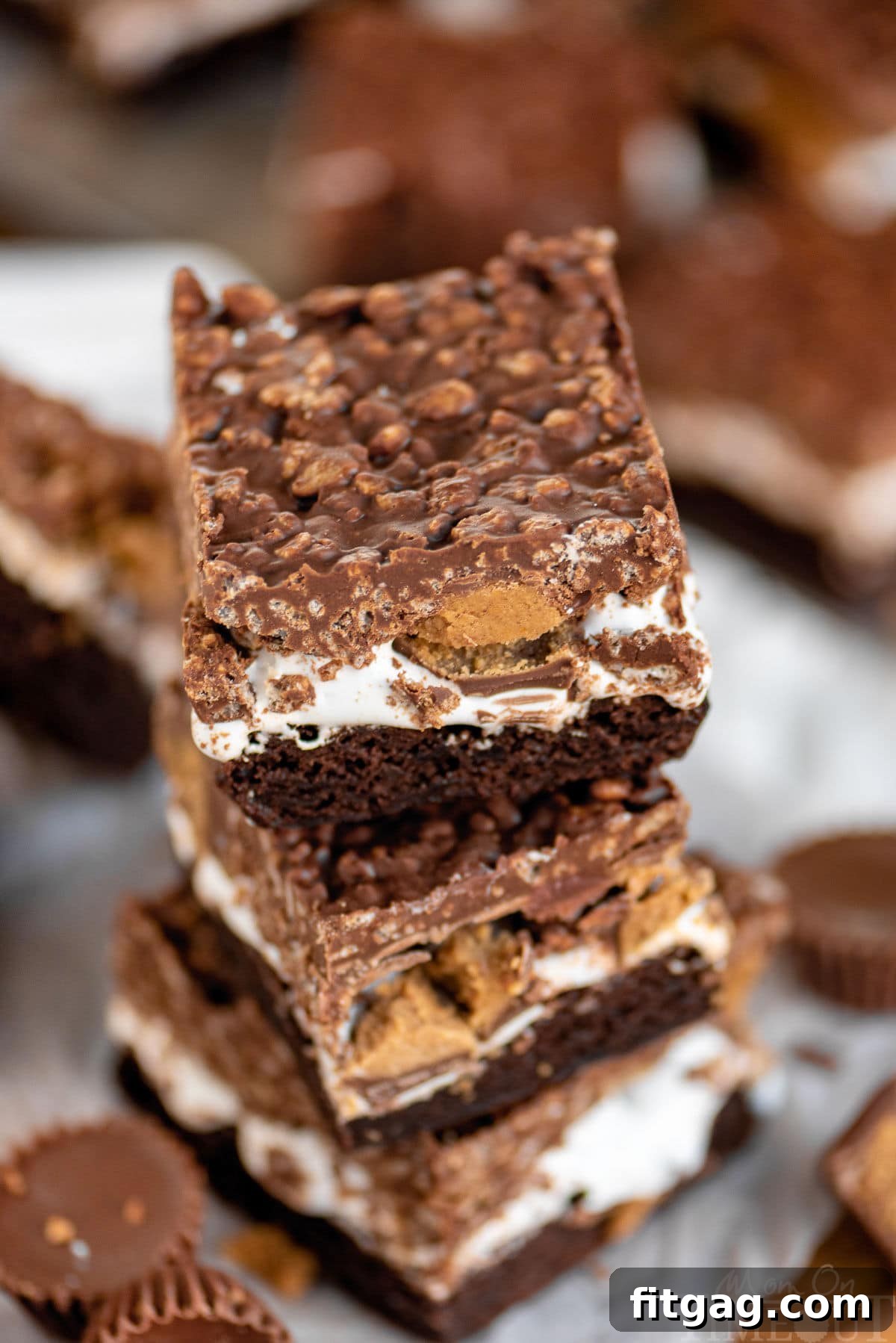 Peanut Butter Cup Marshmallow Brownies 5 An angled top-down view of three stacked brownies, clearly showing the distinct layers of brownie, marshmallow, Reese's, and crispy topping.