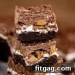 Three brownies stacked on each other showing distinct layers of brownie, marshmallow creme, Reese's peanut butter cups, and a chocolate peanut butter rice krispie topping.