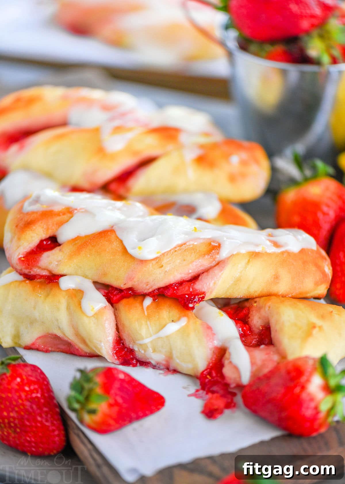 A beautiful side shot of golden-brown Strawberry Twists, generously drizzled with lemon glaze, with fresh strawberries artfully arranged in front.