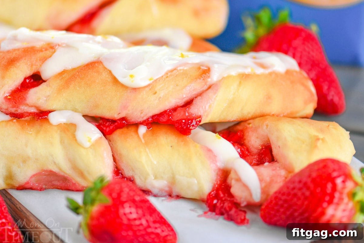 A generous pile of freshly baked Strawberry Twists, glistening with lemon glaze, with fresh, bright red strawberries scattered beside them.