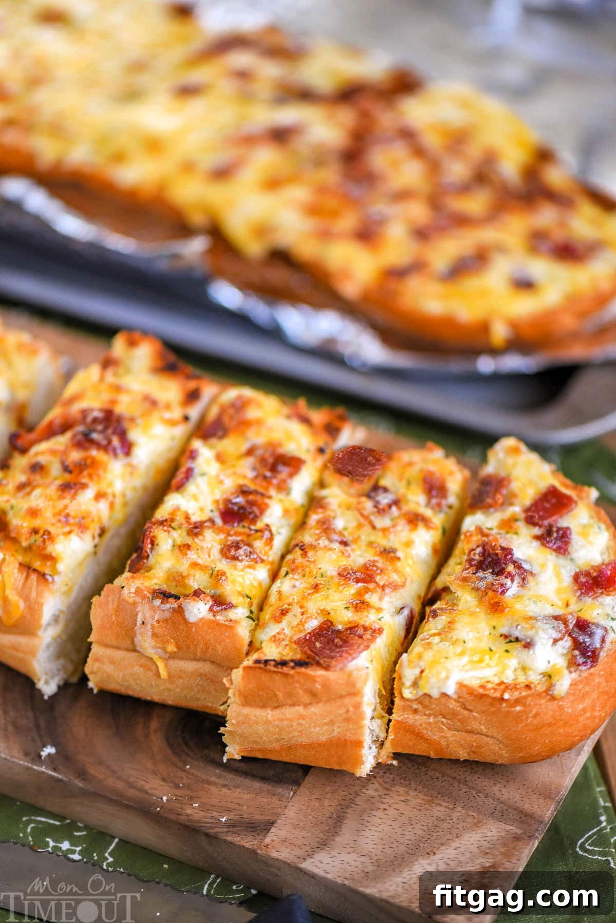 Loaf of cheesy bread made with bacon and ranch resting on wood board cut into pieces ready to be enjoyed.