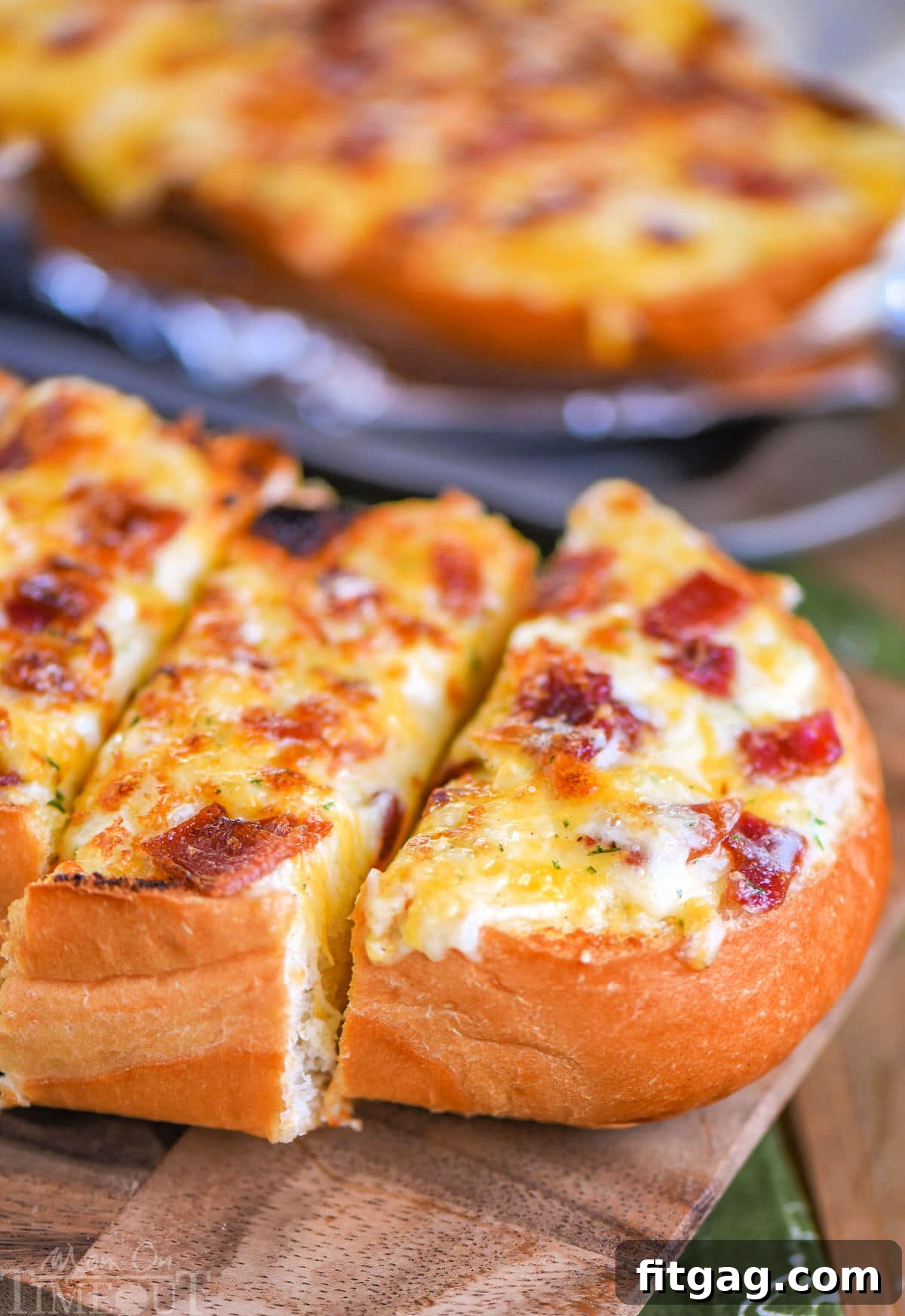 Close up look at loaf of cheese bread made with bacon and ranch. Three pieces have been cut off one half of the loaf on a wood cutting board.