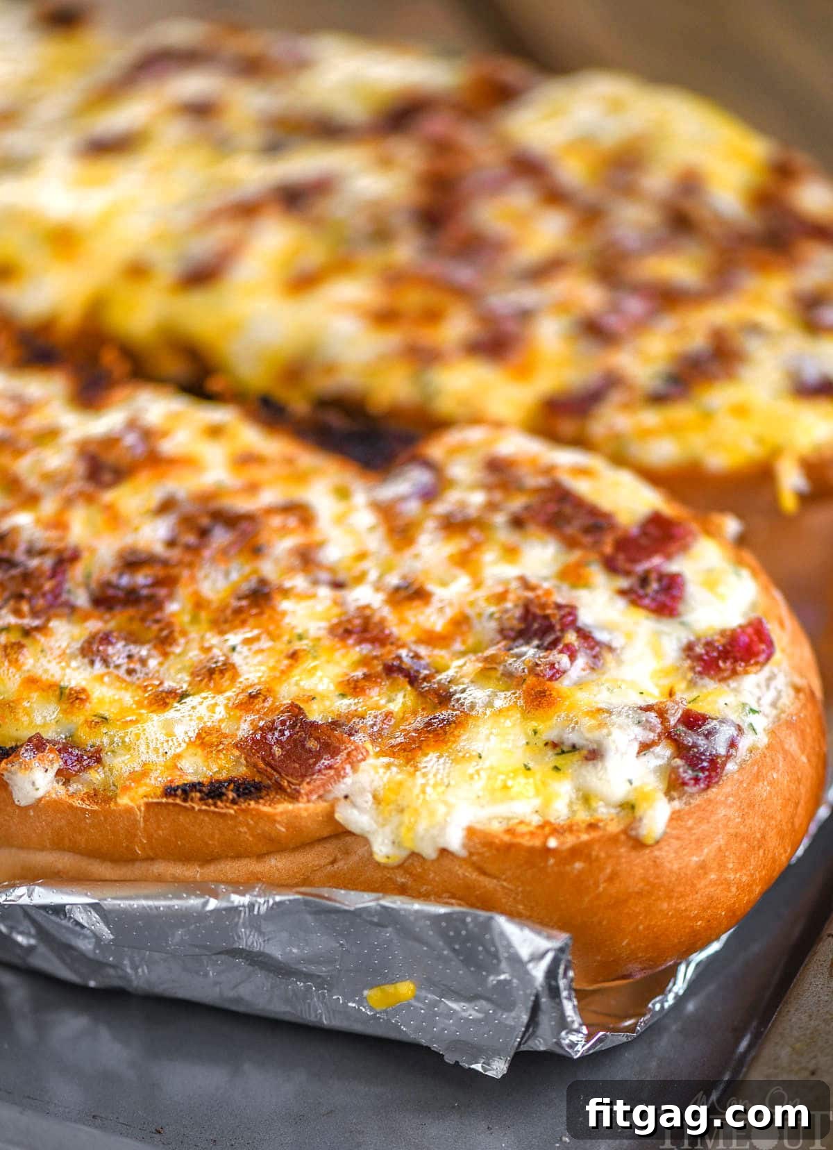 Two halves of a loaf of bread baked up into cheese bread with bacon and ranch. The bread is still on a foil lined baking sheet and has not been cut up.