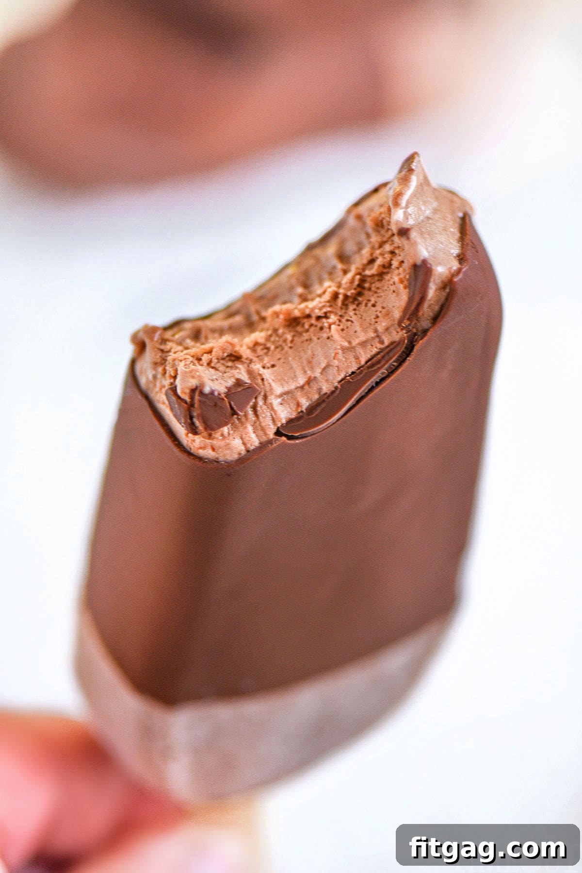 A magic shell-coated fudge bar with a bite taken out, held up to showcase its perfect crackly texture.