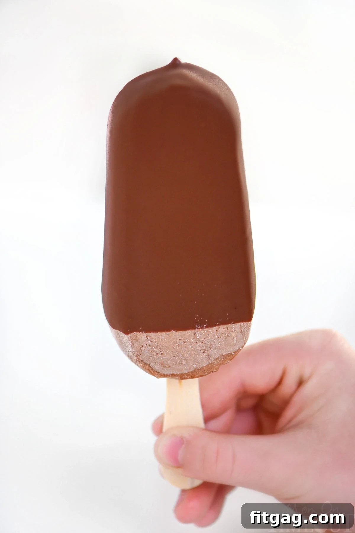 A child's hand happily holding up a fudge pop perfectly coated in homemade chocolate magic shell.