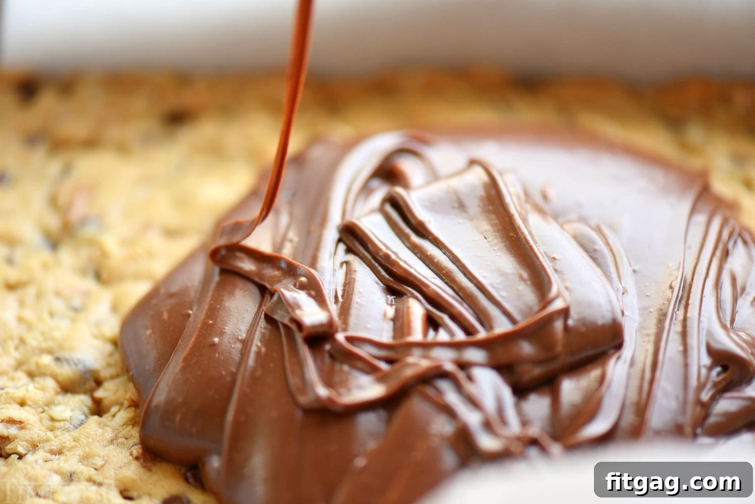 The delicious fudge layer being spread over the partially baked oatmeal chocolate chip cookie base for Monster Fudge Bars.