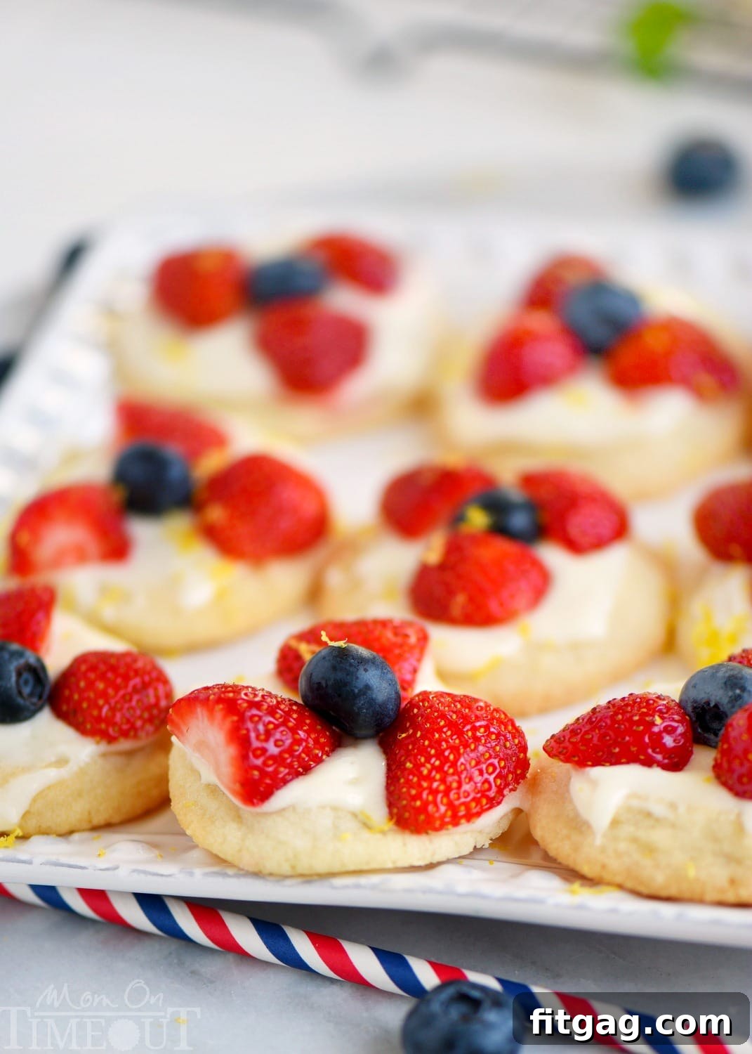 A plate of freshly baked Berries 'N Cream Cookies, garnished with blueberries and sliced strawberries.