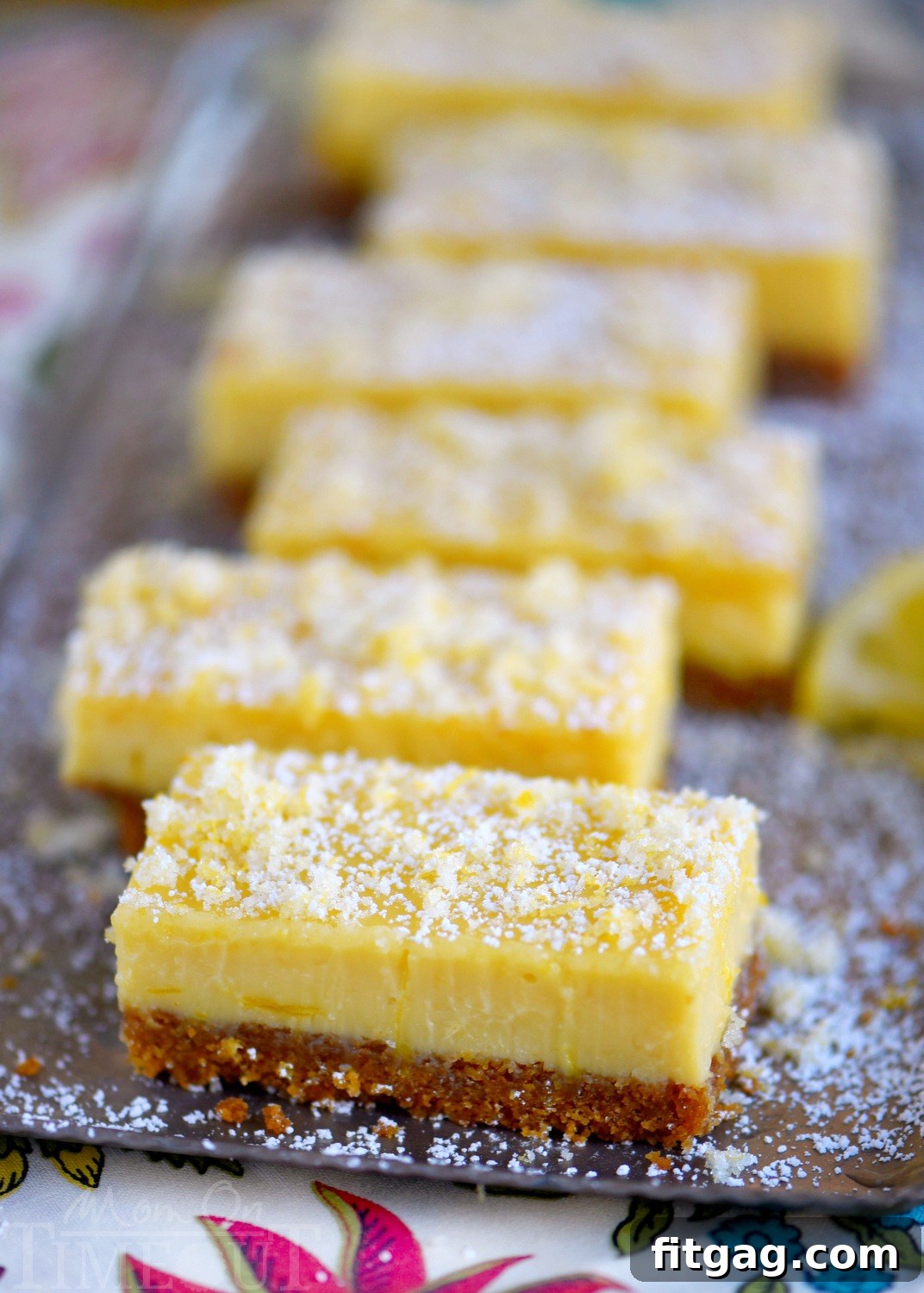 A high-angle view of multiple Lemon Drop Bars on a white surface, garnished with candied lemon zest and powdered sugar.