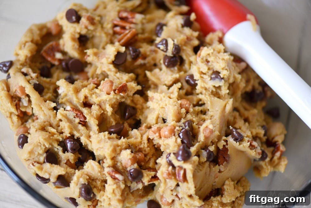 Outrageous Chocolate Chip Turtle Pudding Cookies are loaded with chocolate chips, pecans, and caramel. These giant, bakery style cookies will steal the show! Extra chewy and packed with flavor! A pile of delicious turtle cookies on a white plate.
