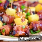 Plate of bacon wrapped chicken teriyaki bites with pineapple. Each bite is skewered with a toothpick and topped with green onions and sesame seeds.