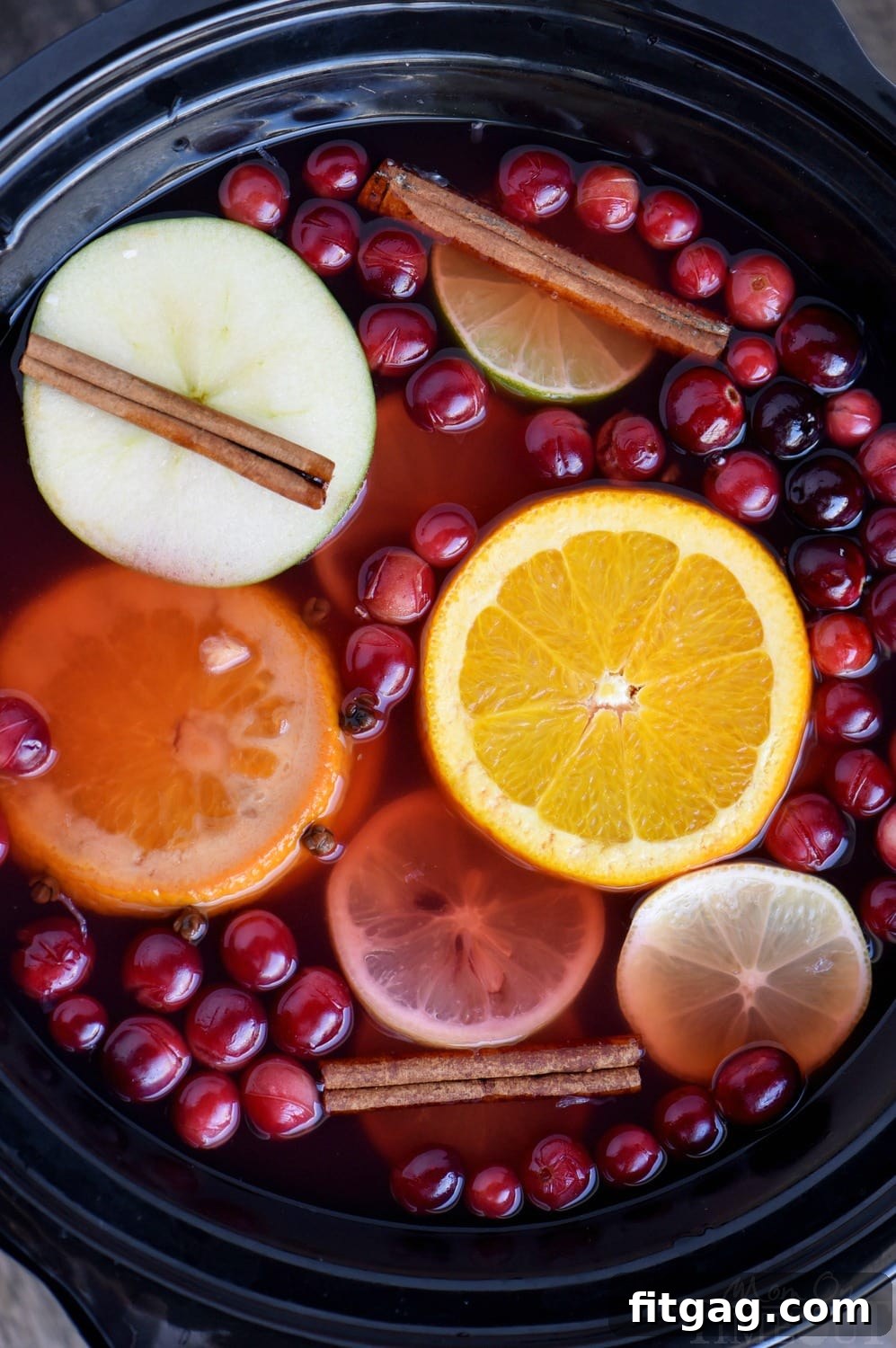 top down view crockpot full of cranberry cider with apple and orange slices and cinnamon sticks and cranberries floating on top