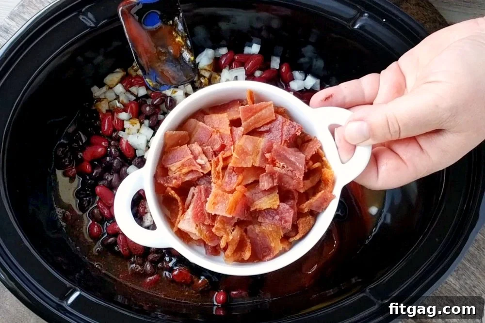 Slow Cooker Kielbasa and Barbecue Beans is the perfect chilly day recipe! Made with three different beans, molasses, bacon, and kielbasa - it's pure comfort food! // Mom On Timeout #slowcooker #crockpot #recipes #bacon #beans #bbq #kielbasa #comfortfood #dinnerideas #recipe Crispy bacon being added to the slow cooker full of barbecue beans.