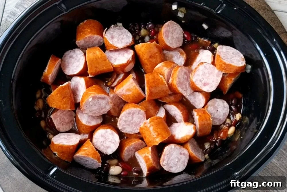 Slow Cooker Kielbasa and Barbecue Beans is the perfect chilly day recipe! Made with three different beans, molasses, bacon, and kielbasa - it's pure comfort food! // Mom On Timeout #slowcooker #crockpot #recipes #bacon #beans #bbq #kielbasa #comfortfood #dinnerideas #recipe All the ingredients for Slow Cooker Kielbasa and Barbecue Beans layered in the slow cooker, ready to cook.