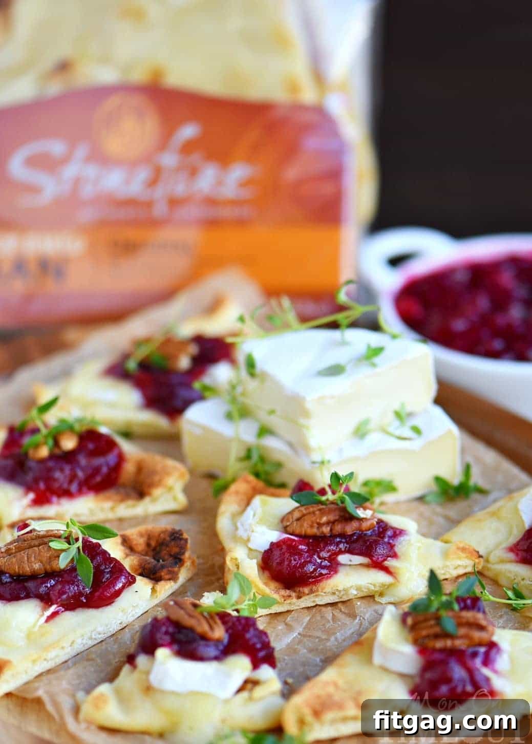 Assembling Cranberry Pecan Brie Bites on a baking sheet with naan, brie, cranberry, and pecans