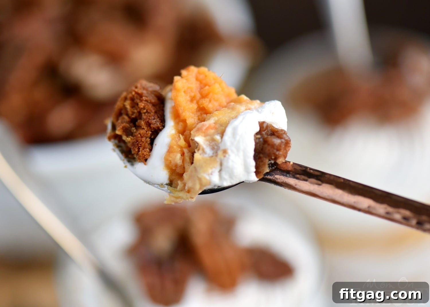 A close-up shot of a spoonful of sweet potato cheesecake parfait, showing off the intricate layers and the textural contrast between creamy and crunchy elements.