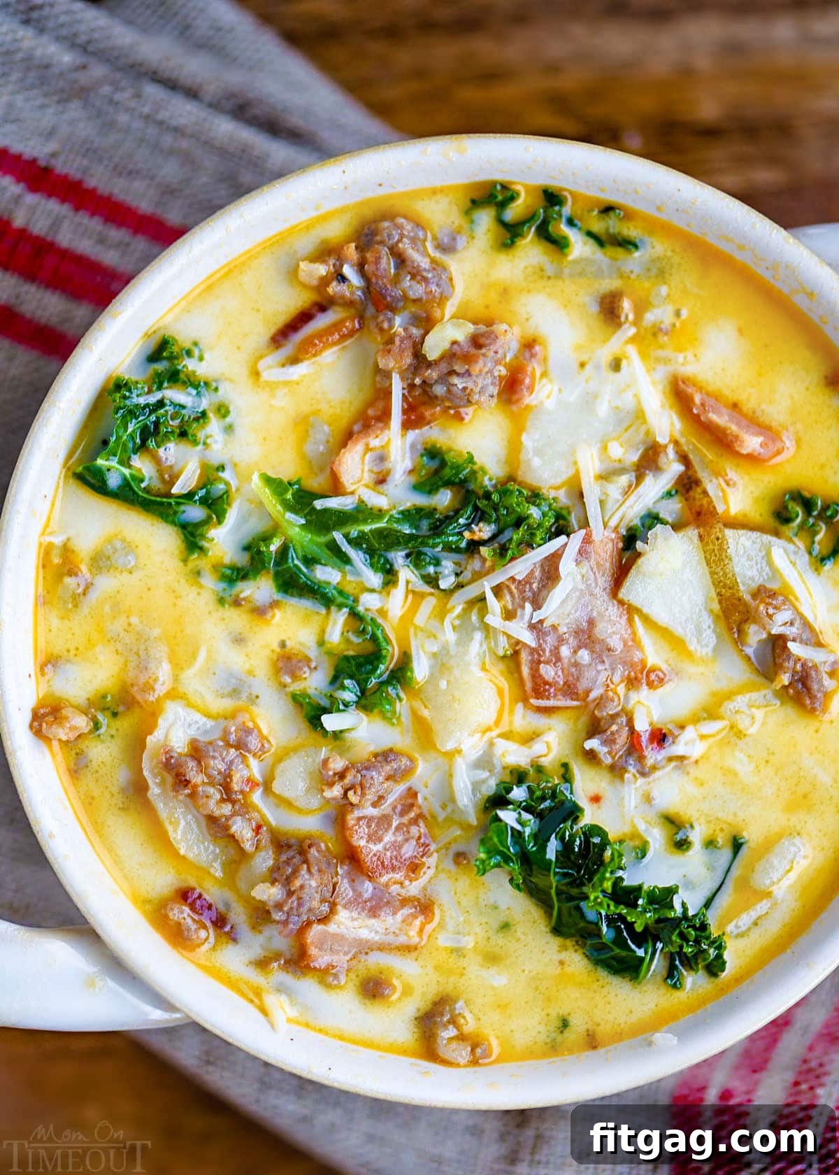 Hearty Tuscan Farmhouse Soup 2 Top-down view of a steaming bowl of Zuppa Toscana soup in a white bowl with handles, garnished with freshly grated Parmesan cheese and sitting on a brown and red linen napkin.