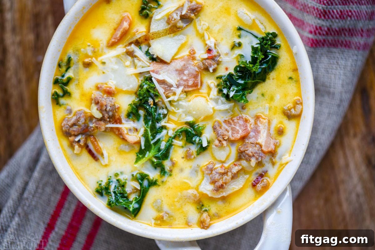 Hearty Tuscan Farmhouse Soup 4 Top-down view of a steaming bowl of Zuppa Toscana soup in a white bowl with handles, garnished with freshly grated Parmesan cheese and sitting on a brown and red linen napkin.