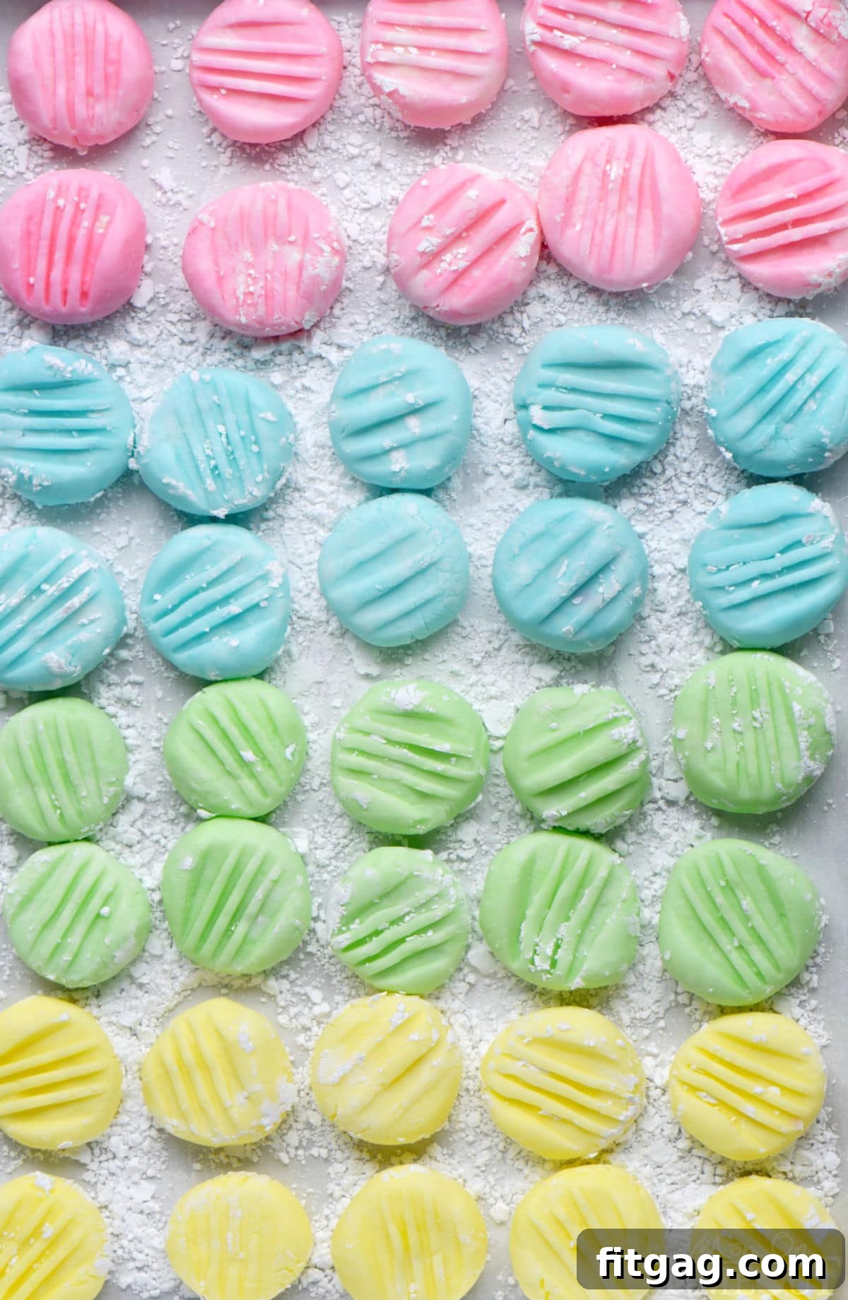 Ultimate Cream Cheese Mints 7 Top down view of recipe for cream cheese mints on parchment paper flattened with the tines of a fork. Four pastel colors are shown: pink, blue, green and yellow in a symmetrical grid layout.