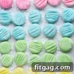Top down view of recipe for cream cheese mints on parchment paper flattened with the tines of a fork. Four pastel colors are shown: pink, blue, green and yellow in a symmetrical grid layout.