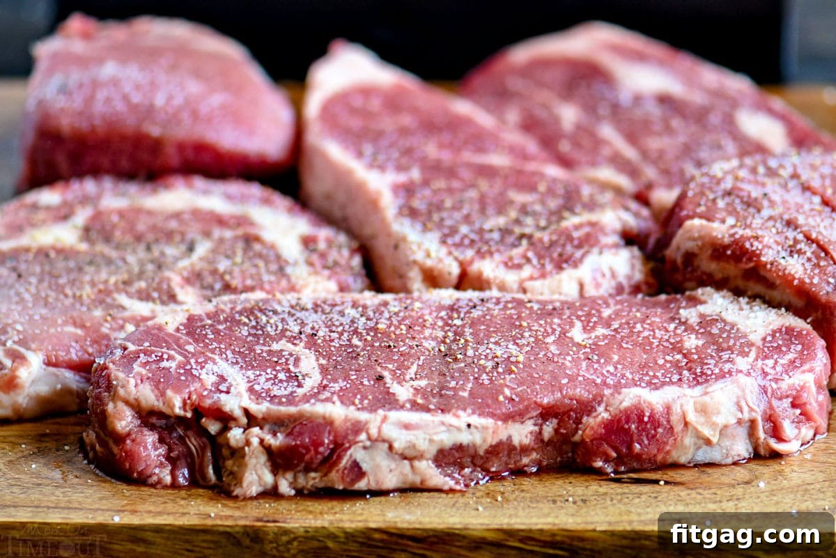 The Ultimate Steak Marinade 3 A variety of raw steaks, perfectly seasoned with salt and pepper, arranged on a rustic wooden cutting board, ready for the marinade.