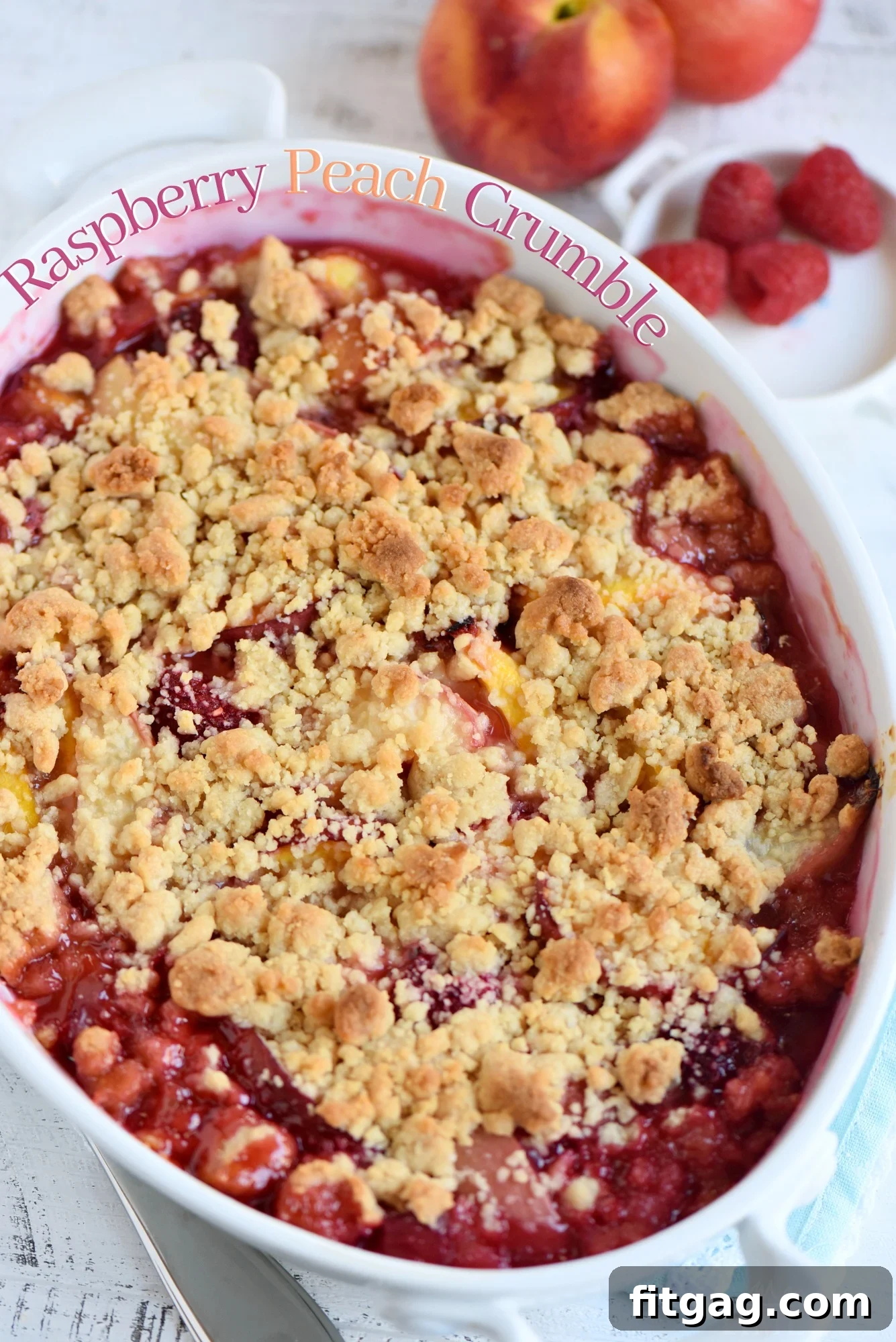 A vibrant Raspberry Peach Crumble in a baking dish, showcasing fresh peaches and bright red raspberries with a golden-brown crumb topping.