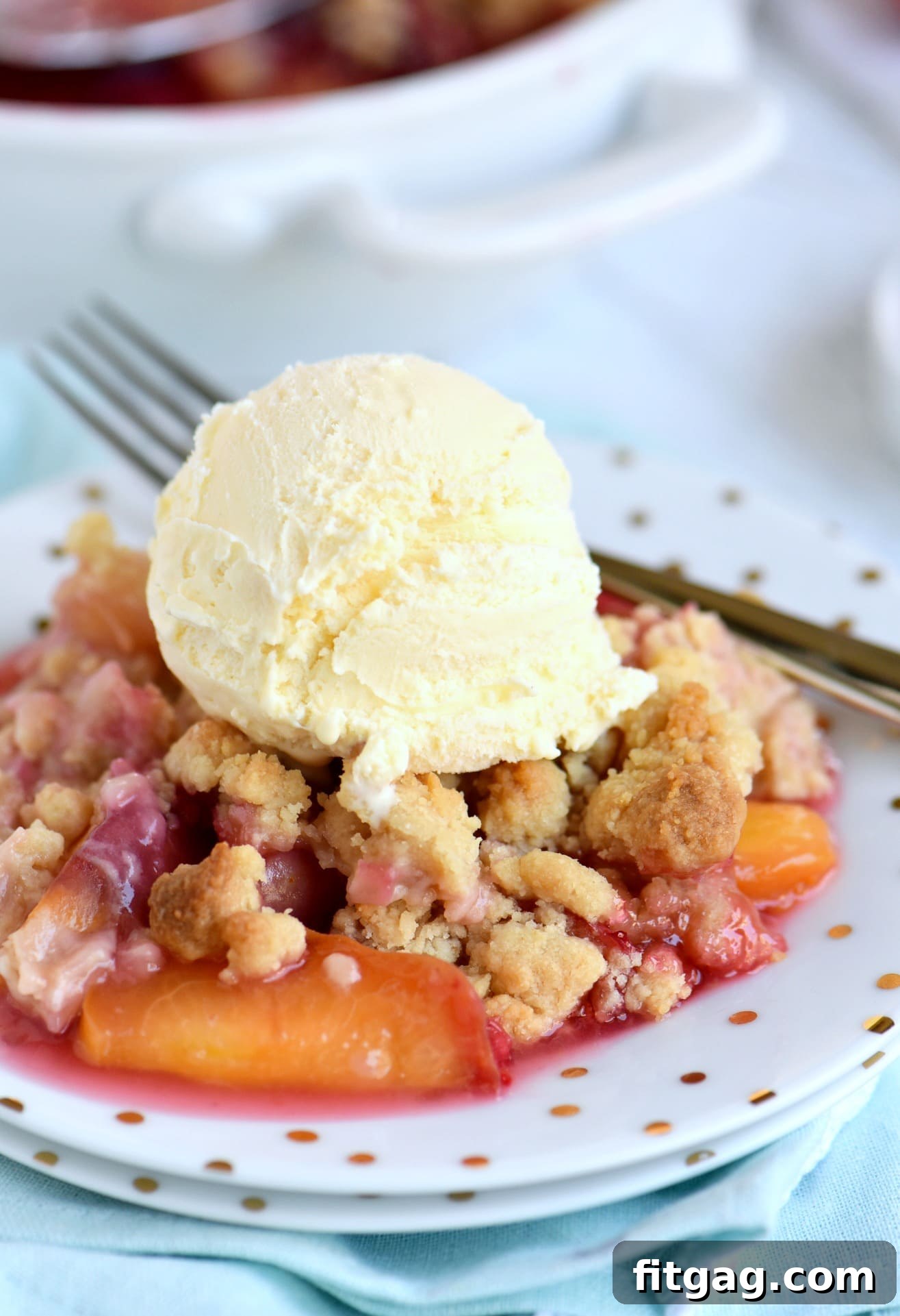A serving of warm raspberry peach crumble topped with a melting scoop of vanilla ice cream on a white plate.